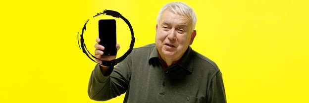 A man with white hair holds up a smartphone, against a bright yellow background. There is an illustrated black brushstroke circling the phone, calling attention to the device.