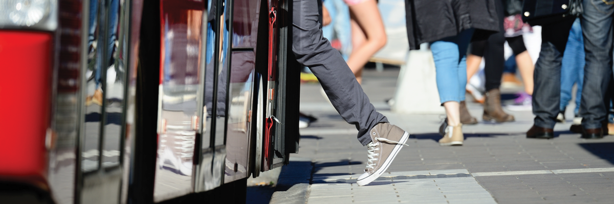 Mid-movement, a person boards a city bus from a sidewalk stop. 