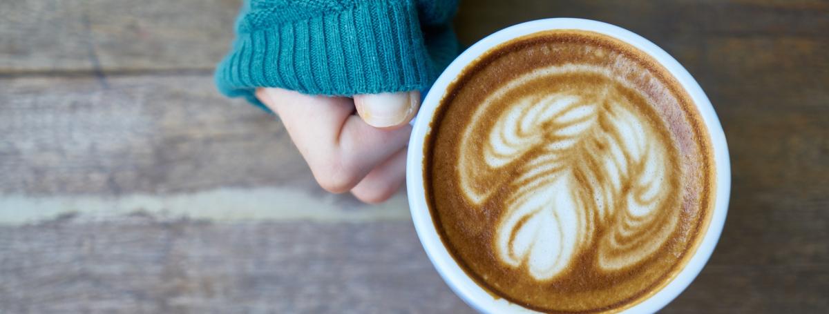 Une main tenant un café latté avec un dessin de coeur dans le lait.