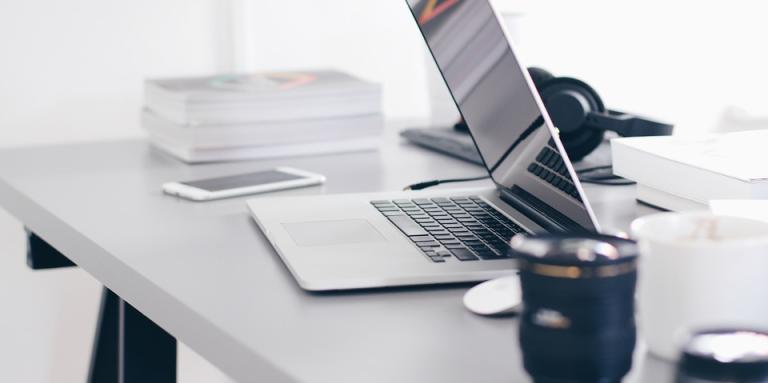 A smartphone, laptop, mouse and mug sitting on a desk.