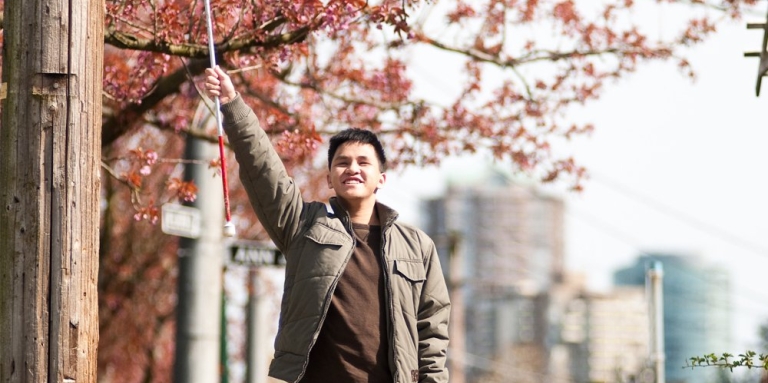 A boy waves his white cane in the air triumphantly.