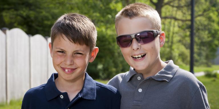 Two young boys smiling and posing outside in front of trees