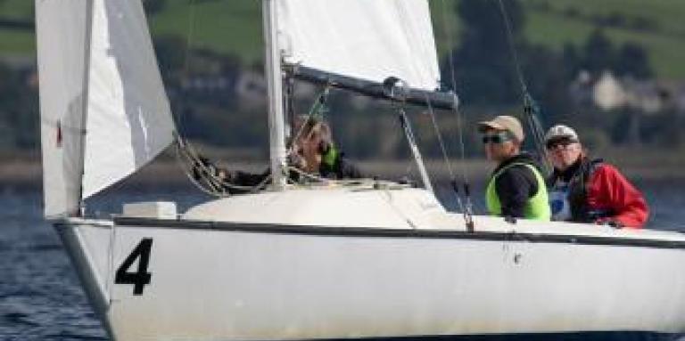 Joshua Cook and two other people sit in a sail boat on the water. They are at the World Blind Sailing Championships in Scotland.