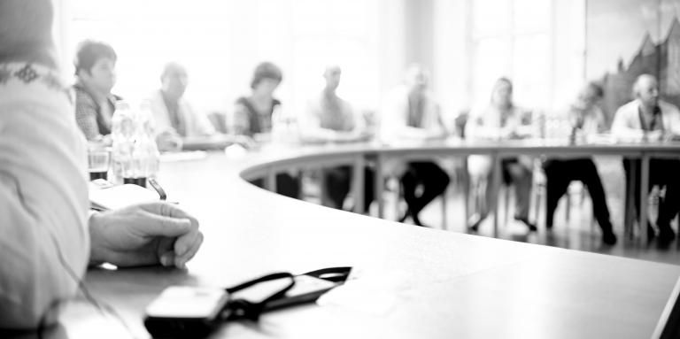 Photographie en noir et blanc de personnes réunies autour d'une table ronde et discutant de différents sujets.