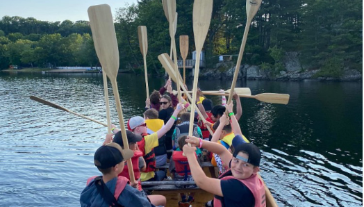 Canoeing on lake joe! Children and youth sit in the Voyageur canoe and hold their paddles high up in the air. 