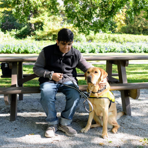 Adam est assis à côté de son chiens compagnons d’INCA, Henson, sur un banc public.