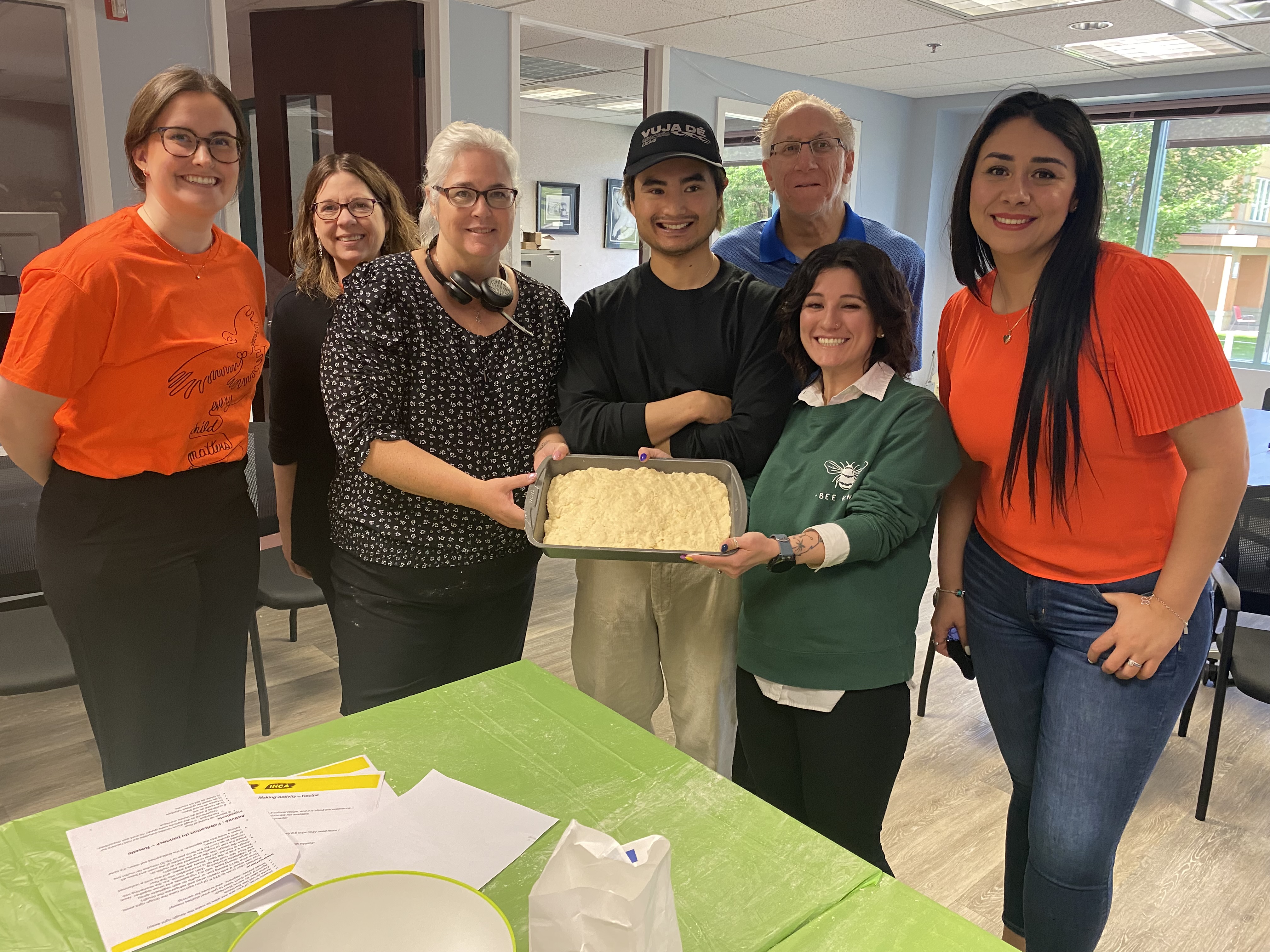 Plusieurs membres du personnel d'INCA sourient en montrant une casserole de pain Bannock qu'ils sont en train de préparer. 