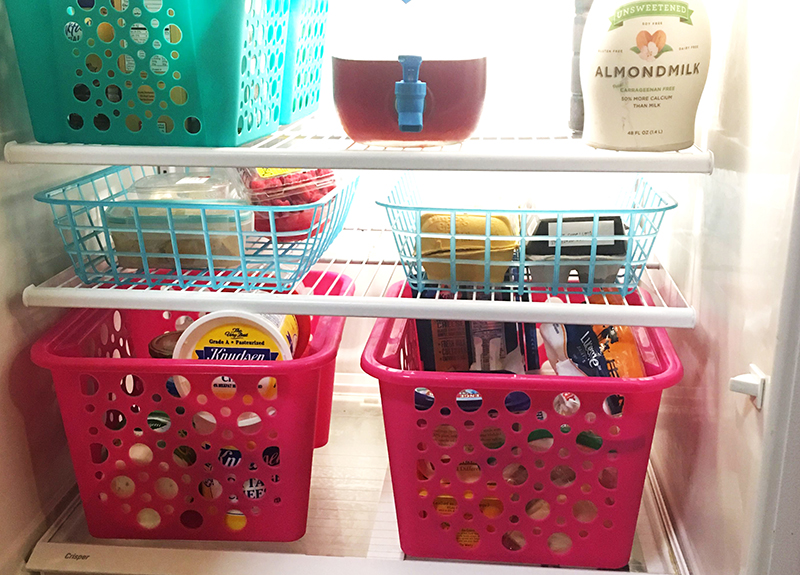 Inside of a fridge filled with brightly coloured plastic baskets containing small food items 