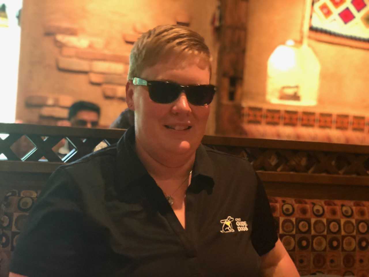 Ashley Nemeth smiles while sitting in a restaurant booth and wearing sunglasses.
