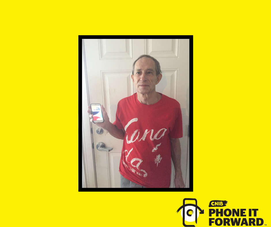 Bill Chadd poses for a photo with his iPhone. He is wearing a red Canada t-shirt standing in front of a door while smiling and holding a iPhone in his right hand.