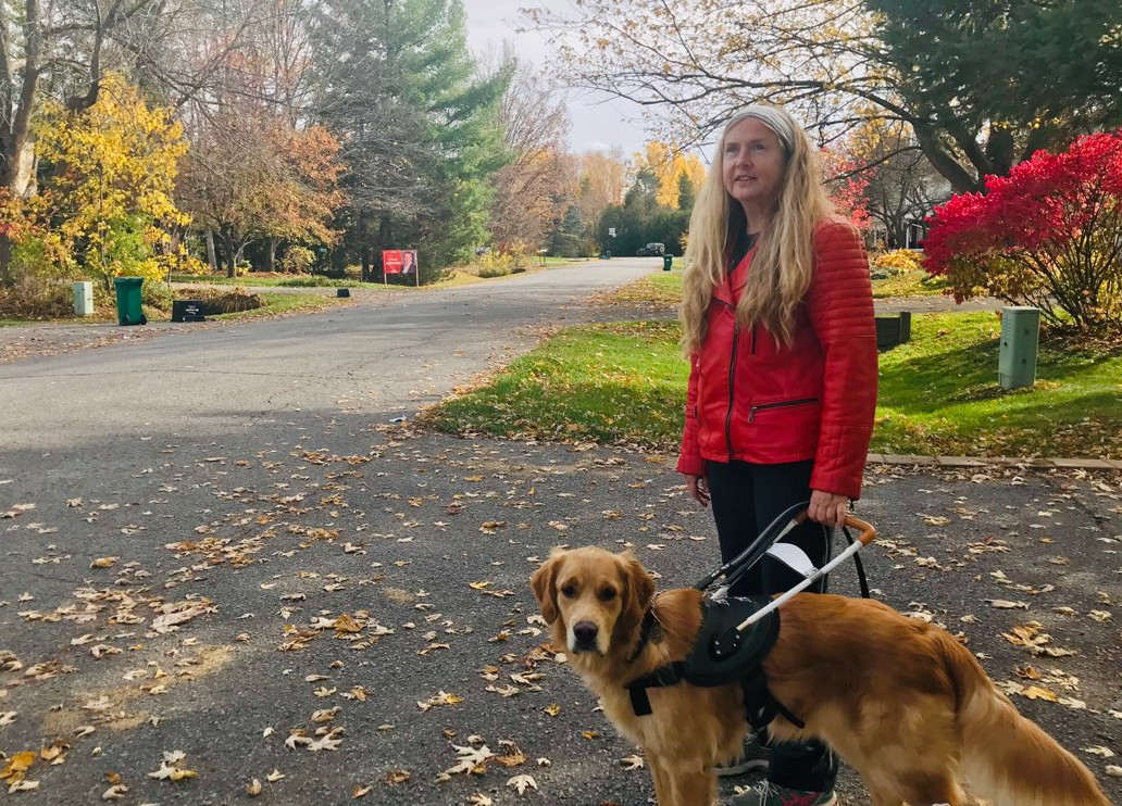 Diane Bergeron walks alongside her guide dog, Carla. Carla is in harness and standing to the left of her.