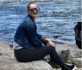 Emilee sitting on rocks beside water with a big smile on her face. 