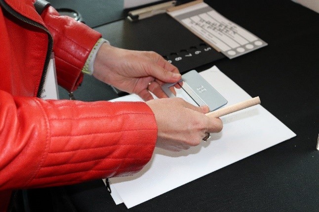 A woman holds a signature guide over a white page with a ballot and tactile ballot overlay beside her.