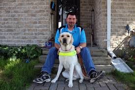 Guy sitting on the front steps of his home with his guide dog sitting between his legs.