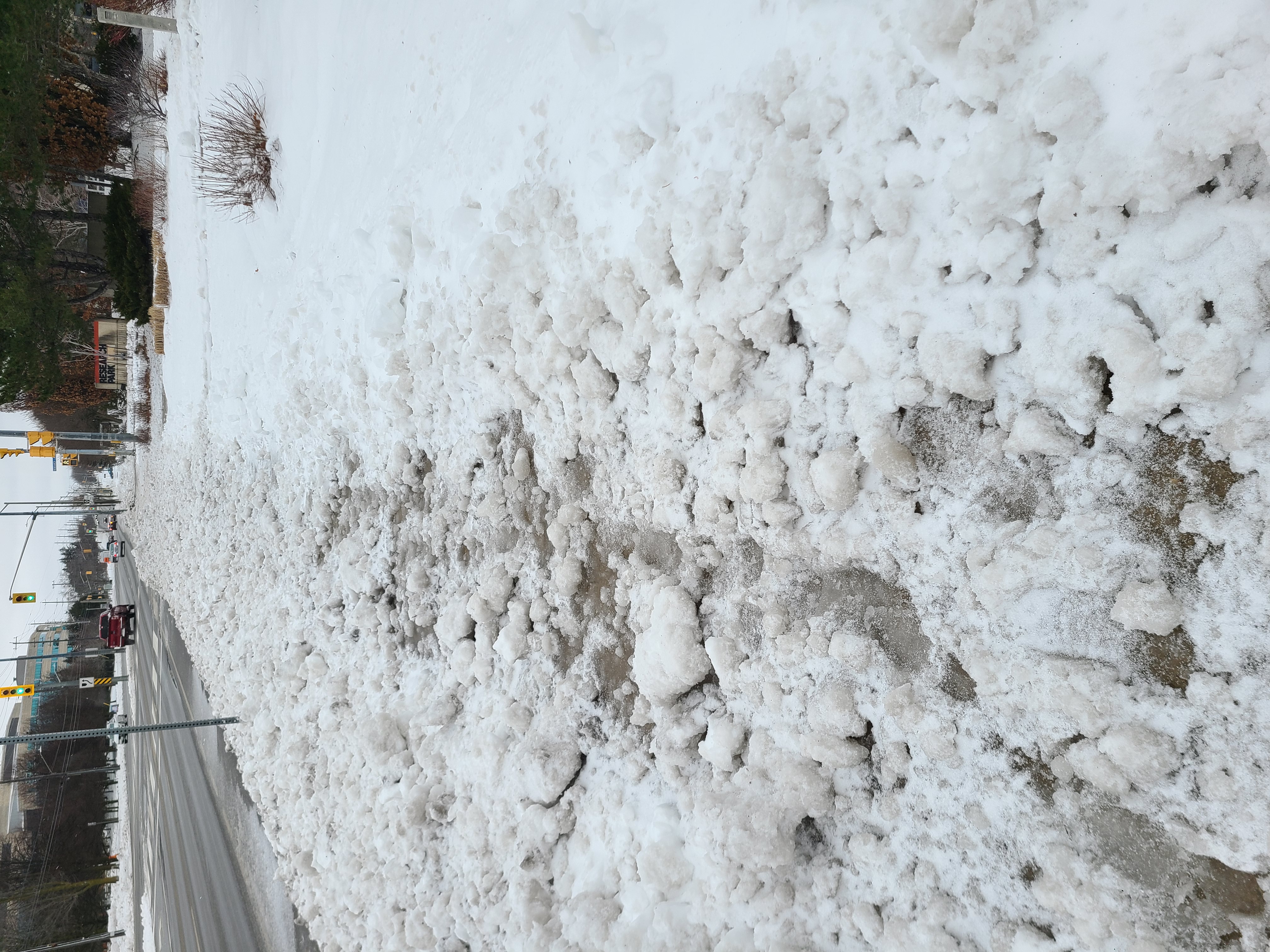 Un trottoir de Guelph qui n'a pas été déneigé. Le trottoir est couvert de monticules de neige et de neige fondue et se trouve près d'une intersection. 