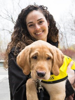 Headshot of Andrea holding a yellow Labrador puppy in a yellow vest.