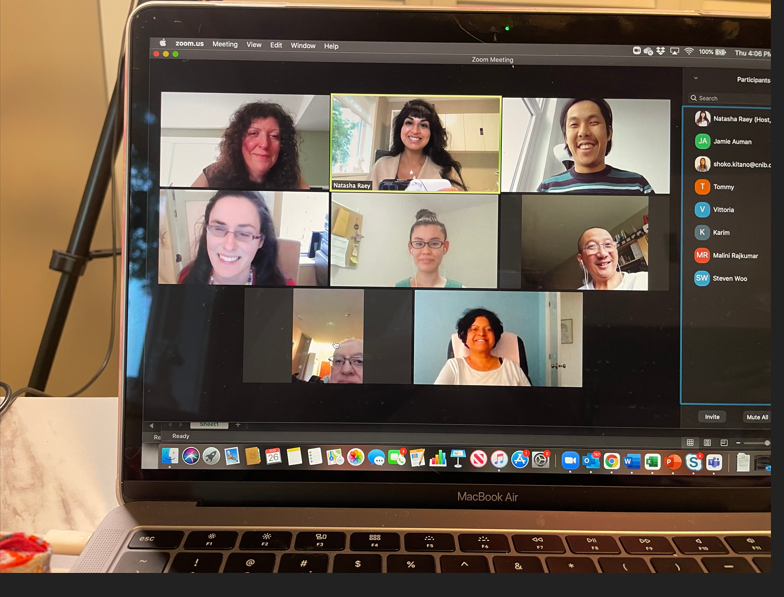 A Zoom call with eight participants is displayed on a laptop screen