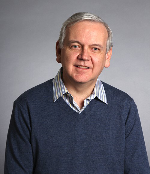 Photo of Jim Maher sitting in front of a grey background.