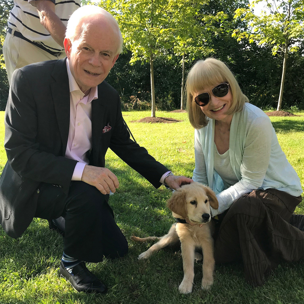 John and Mary Crocker kneel beside a golden retriever puppy on the grass