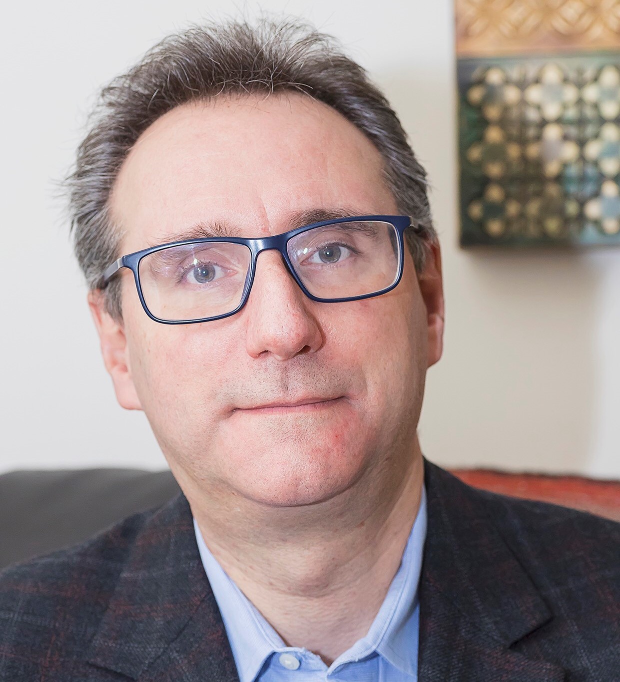 Un portrait de Joshua Simmonds portant des lunettes et un complet