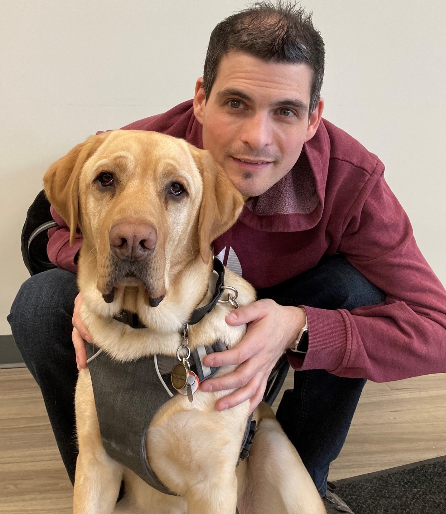 Ryan Hooey is crouched behind his Golden Labrador guide dog, Joe.