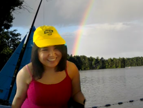 Devant un arrière-plan virtuel d'un lac surmonté d'un arc-en-ciel, Najla pose avec sa casquette jaune de la Fondation INCA, le sourire aux lèvres.