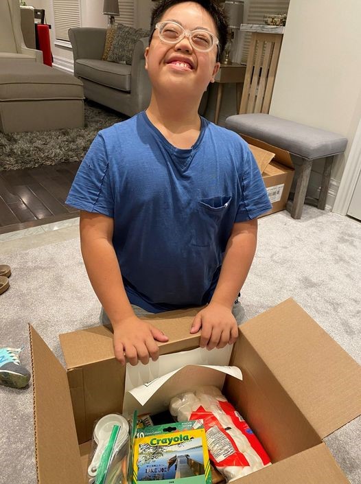 a young camper kneels behind his opened camp box, a huge smile on his face