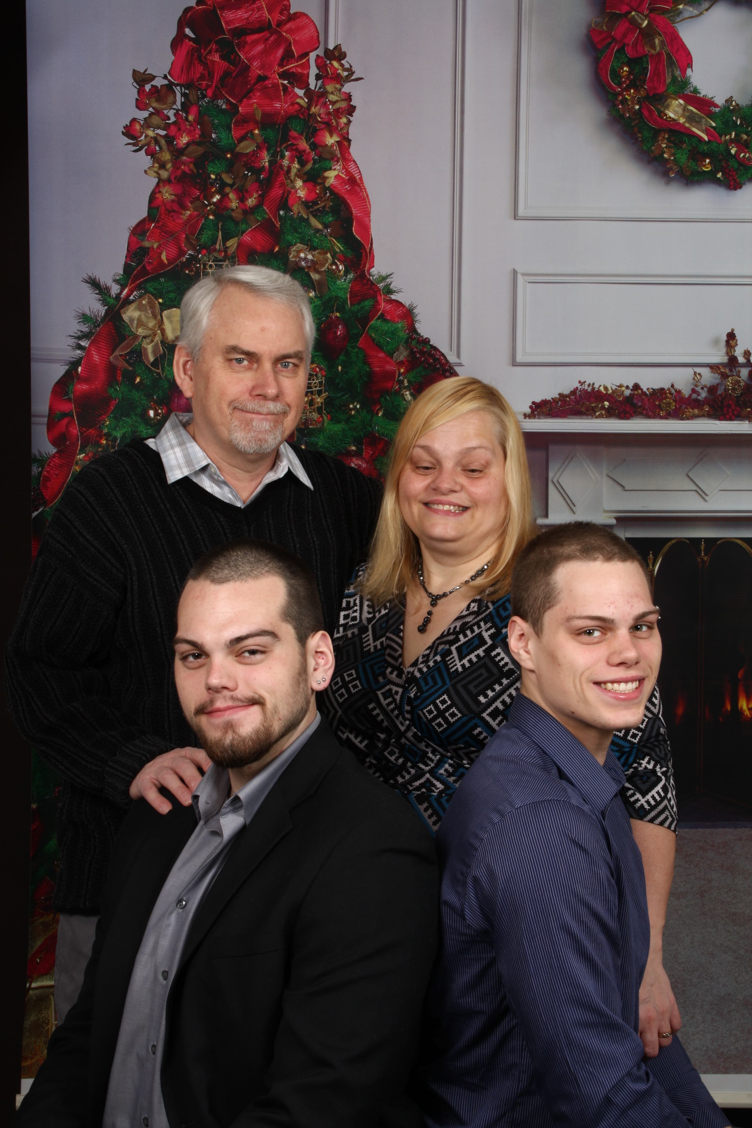 A family Christmas card photo. Rhonda, her husband, and her two adult boys pose for a portrait. A Christmas tree and wreath are displayed in the background.
