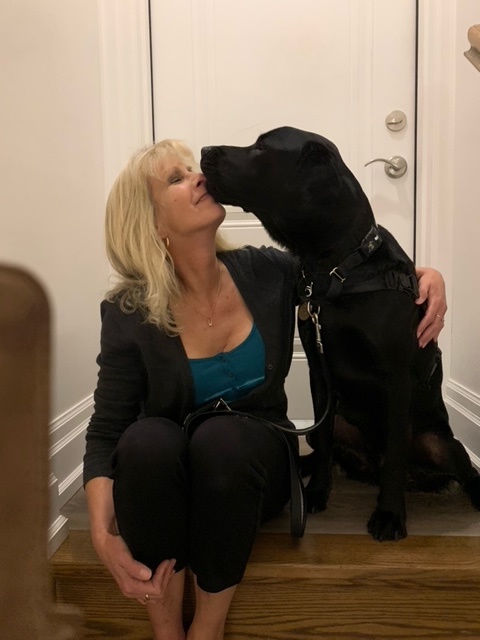 Karen sitting on her steps getting a kiss on the face from Healey, her CNIB Guide Dog. 