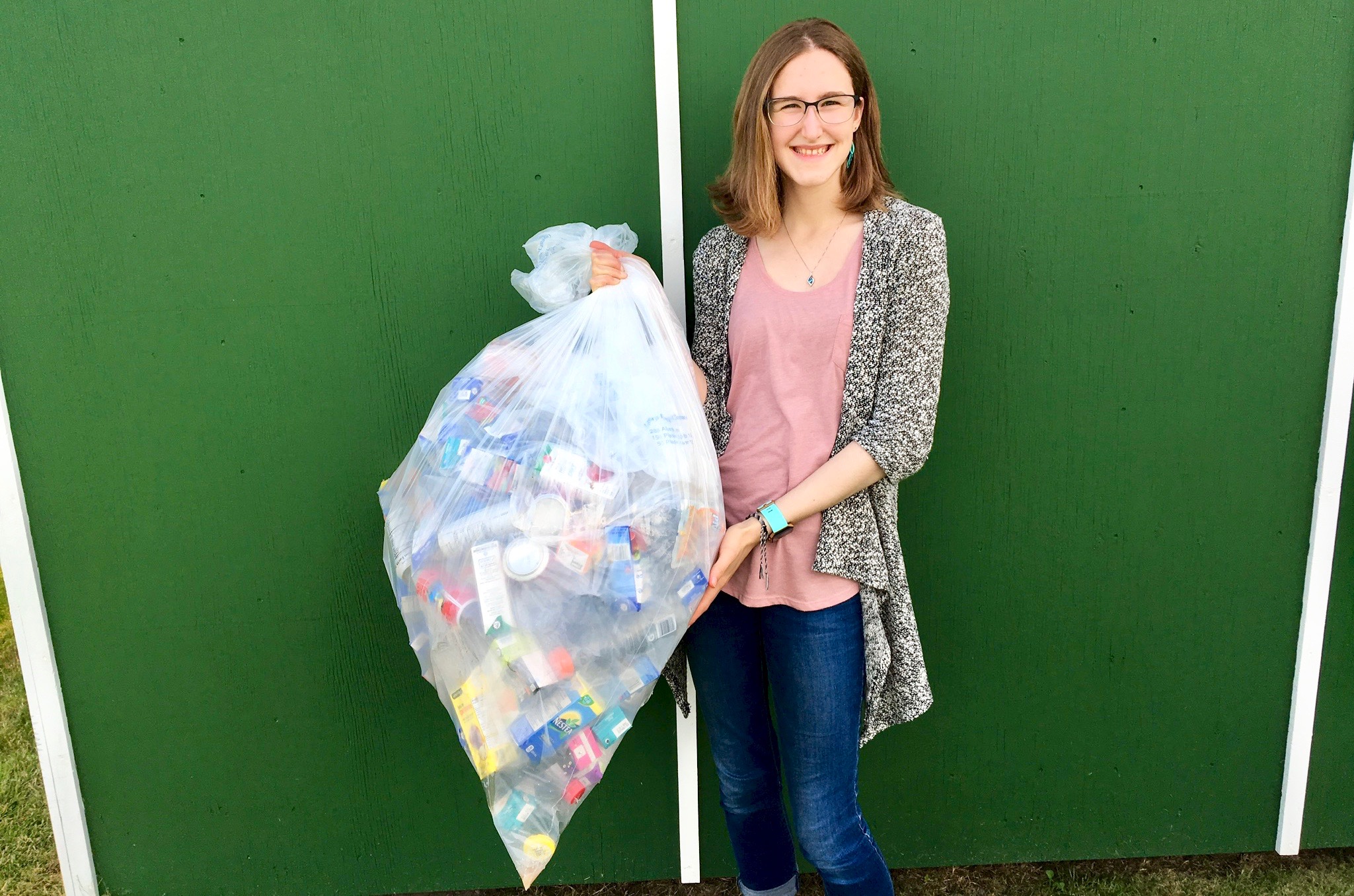 A teenage Veronika holds a white trash bag filled with recycled bottles. 