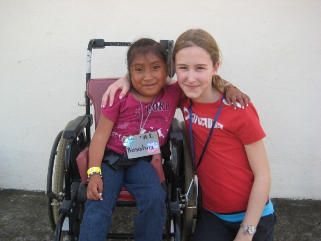 In Guatemala, a young Veronika crouches down next to a girl in a wheelchair. They have their arms around one another and pose for the photo.