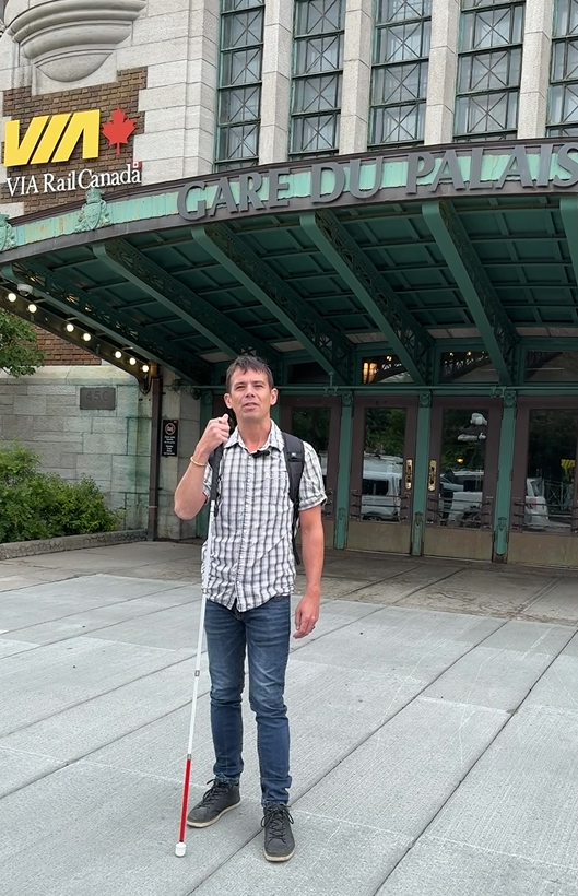 Un homme tient sa canne devant une gare Via rail