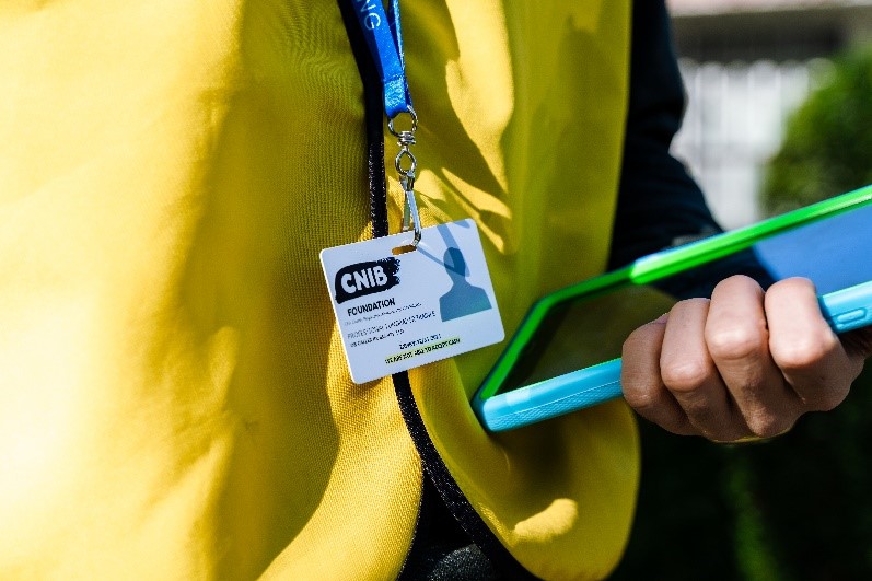 A close view of a CNIB Fundraiser’s yellow vest, ID badge and fundraising tablet.