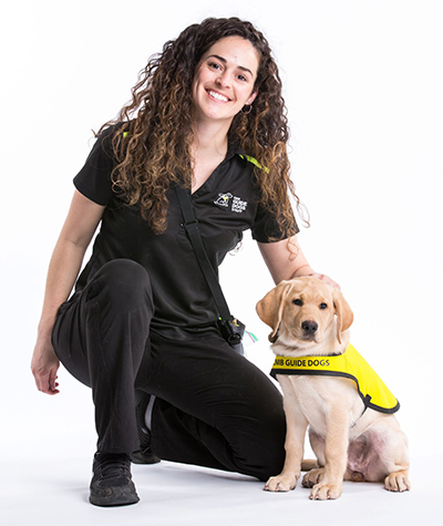 CNIB Guide Dogs trainer kneels next to puppy wearing yellow vest 