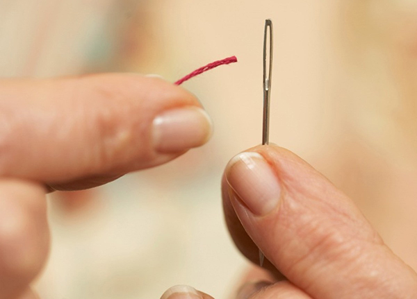 Close-up of person's fingers threading a small needle 