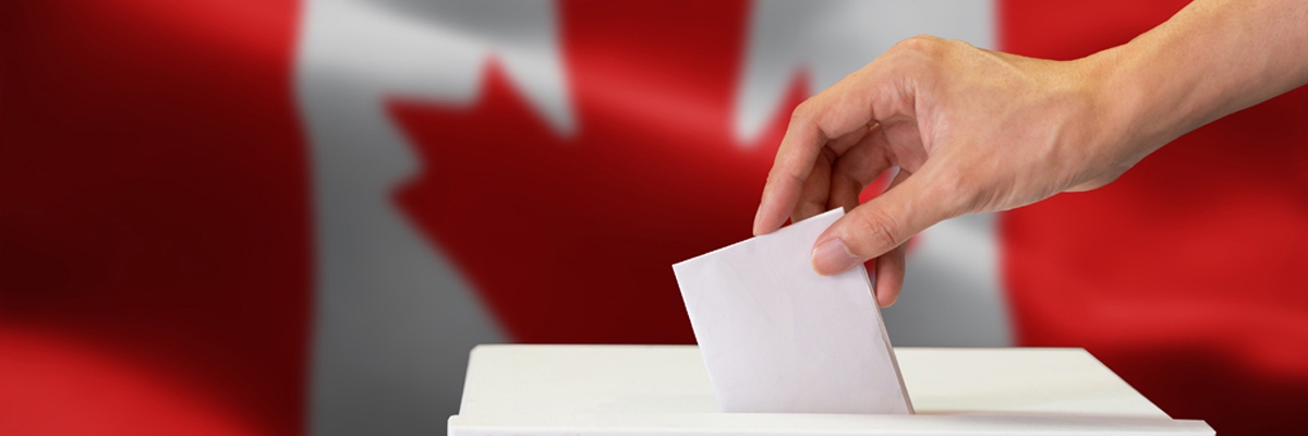 Une personne dépose son bulletin de vote dans une boîte de scrutin. Un drapeau canadien en arrière-plan.