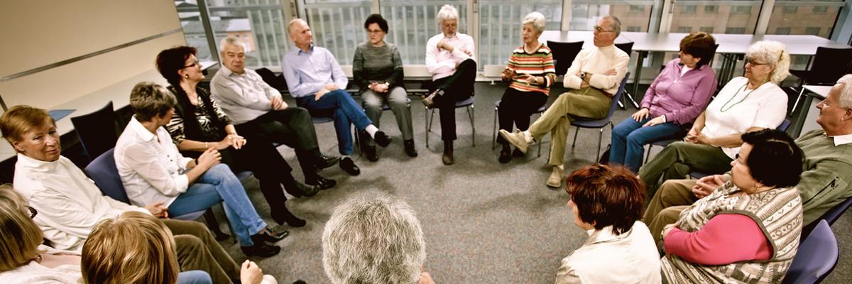 A large group of 17 people gather in a support group. They are seated in a circle.
