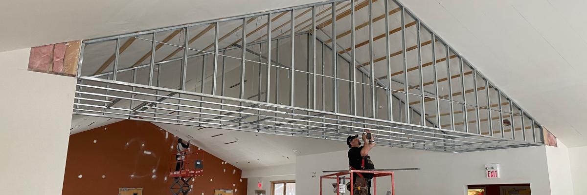 The Dining Hall & Lounge at CNIB Lake Joe. A construction worker stands on a large lift to reach the ceiling with a tool. 