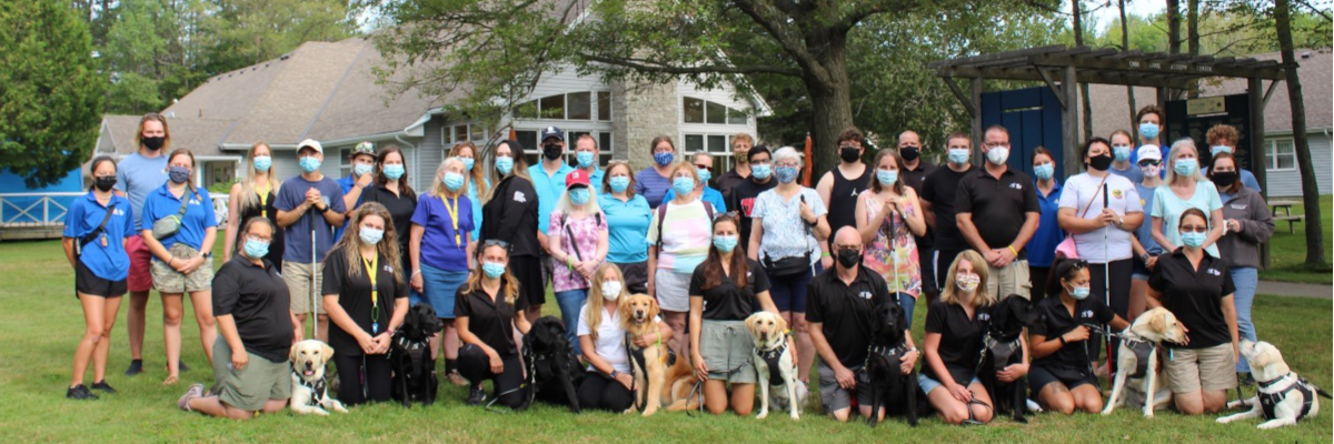 Participants, staff, and guide dogs posing together on the CNIB Lake Joe lawn.