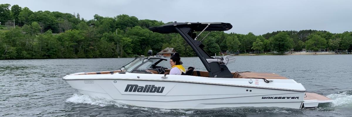 White water ski boat on the lake with the word "Malibu" and "Wakesetter" on the side.