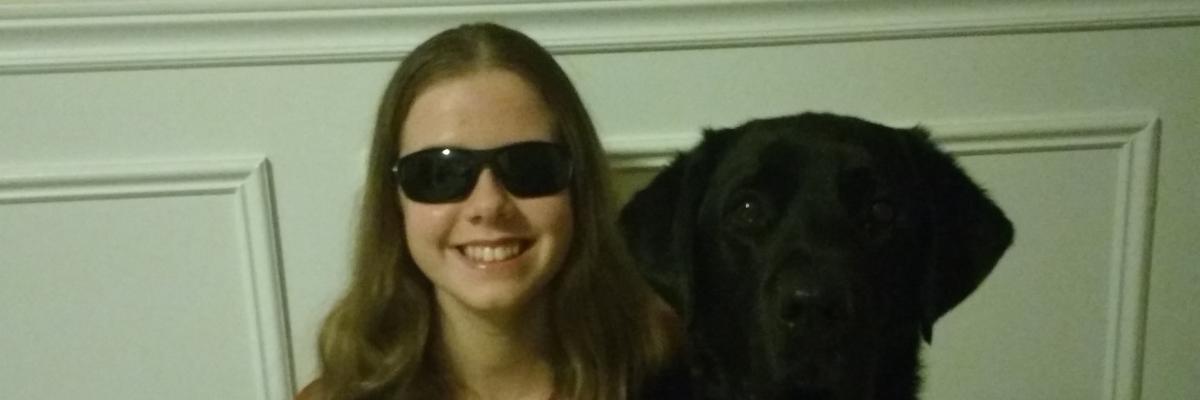 Teen girl with sight loss smiling and wrapping arm around her guide dog