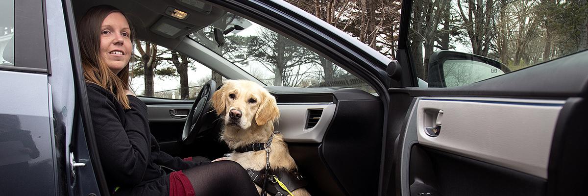 Une femme et son chien-guide, un Golden Retriever, assis dans le siège du passager d’une voiture.