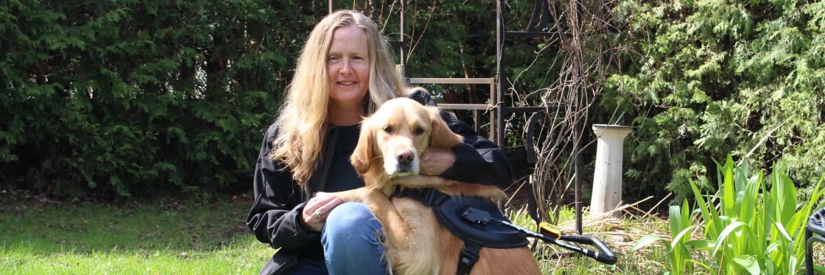 Diane Bergeron à genoux dans l'herbe à côté de son chien-guide Carla, un golden retriever.