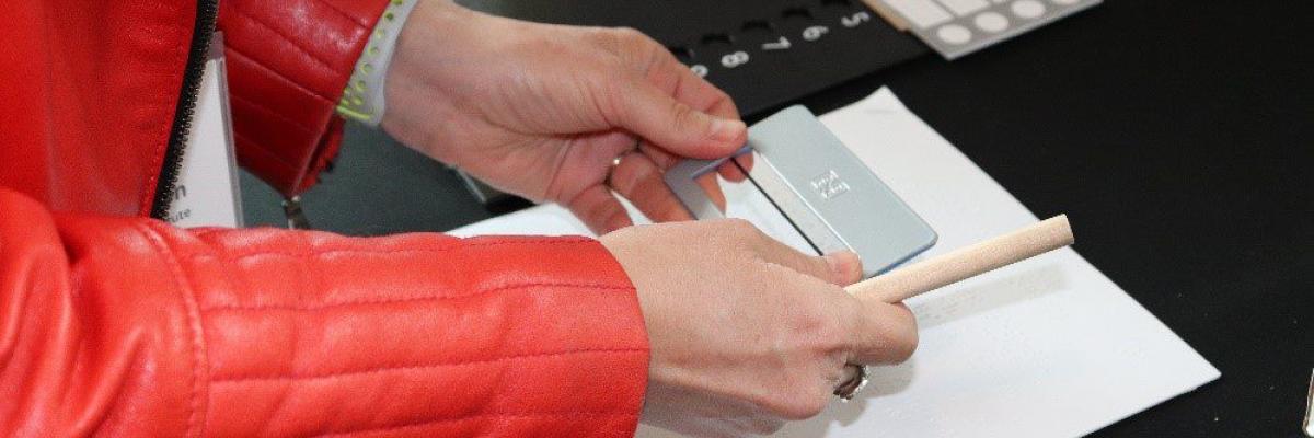 A Canadian woman holds a signature guide over a braille document. A tactile voting template is beside her.