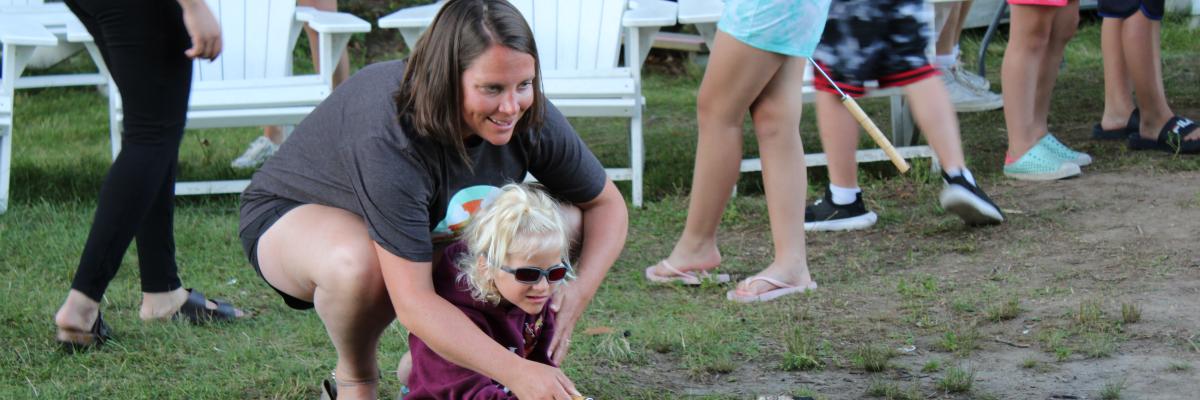 A mother and daughter roast a marshmallow over a campfire at CNIB Lake Joe. 