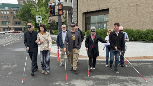 Claude les yeux bandés guidé par Valérie directrice d’INCA Québec, Pierre-Luc les yeux bandé guidé par Jean-Michel et un bénévole derrière lui, Maude guidée par David et René du RPHV 03-12 à l’arrière traversent la rue en direction de la caméra en balayant leur canne-blanche devant eux