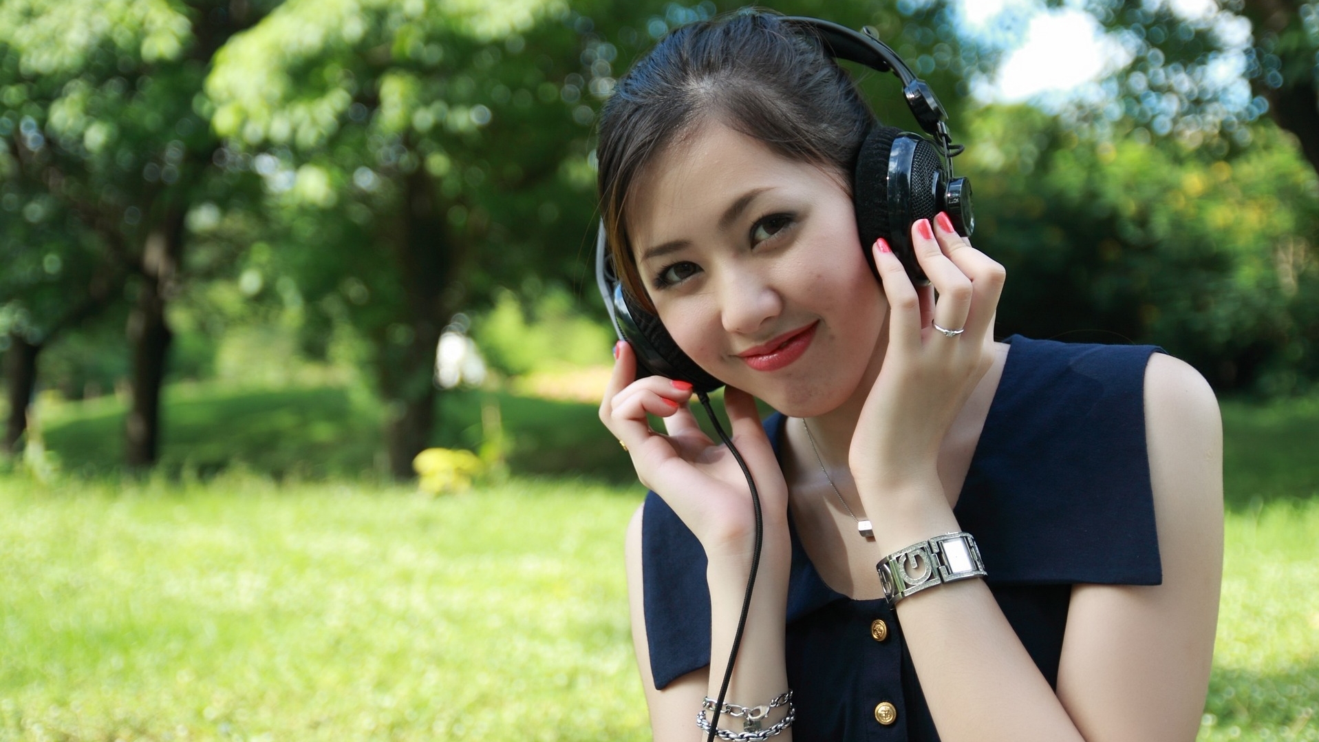 Une fille dans un parc porte un casque d'écoute et sourit.