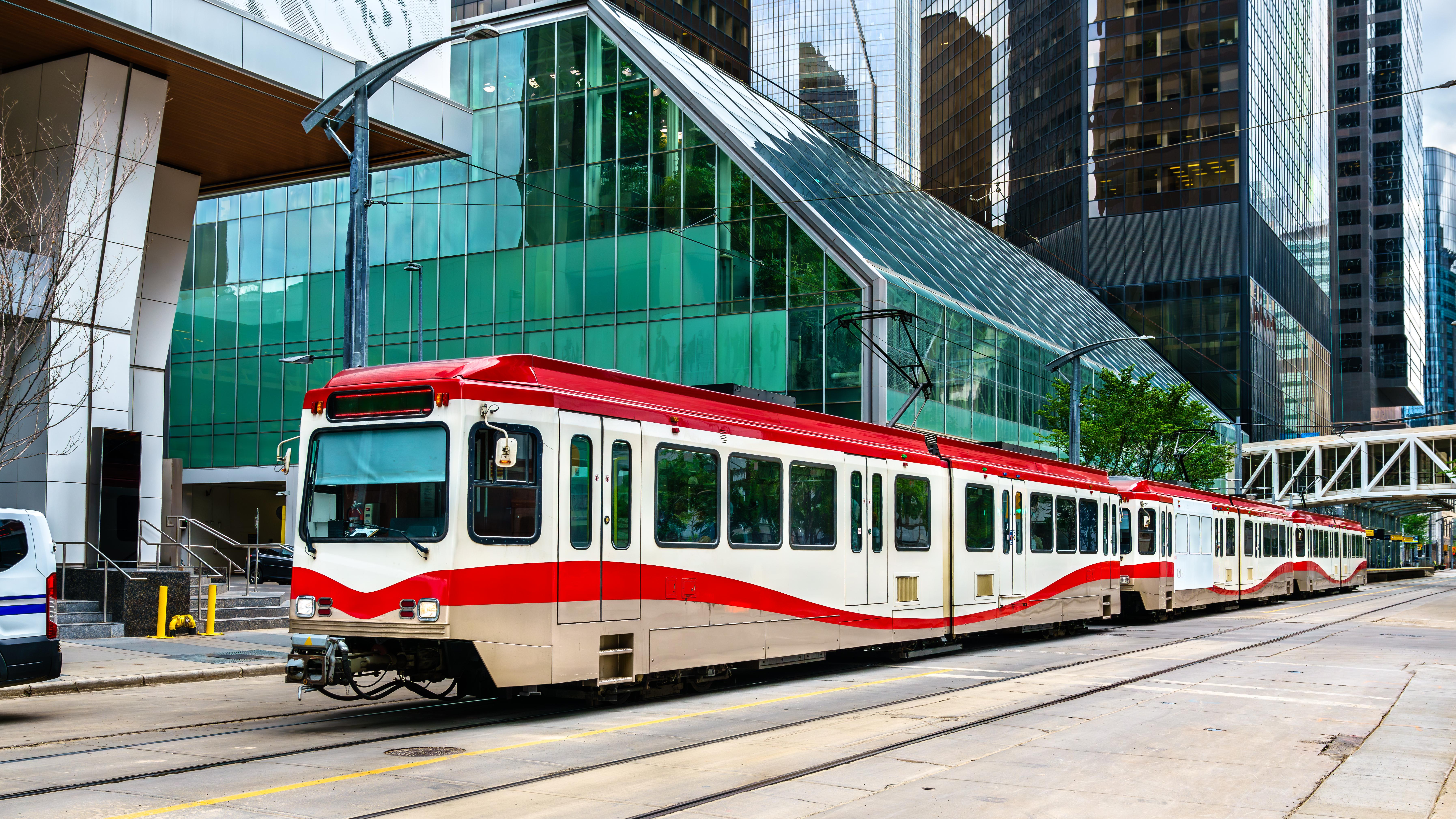 A red and white CTrain car glides along an outdoor light rail track in downtown Calgary. 