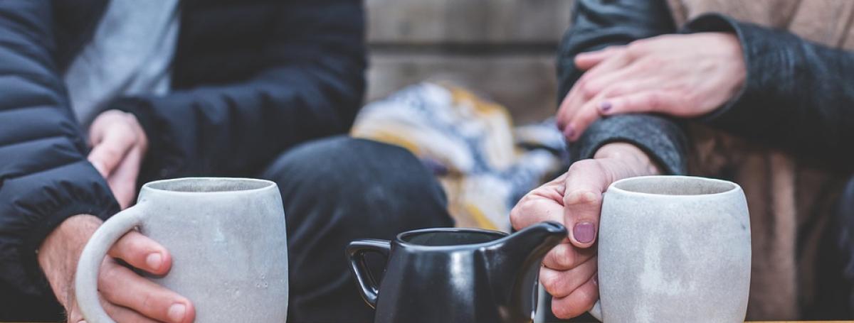 photo of two people seated at a table holding coffee mugs.