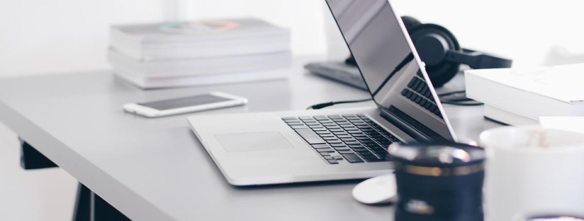 A smartphone, laptop, mouse and mug sitting on a desk.